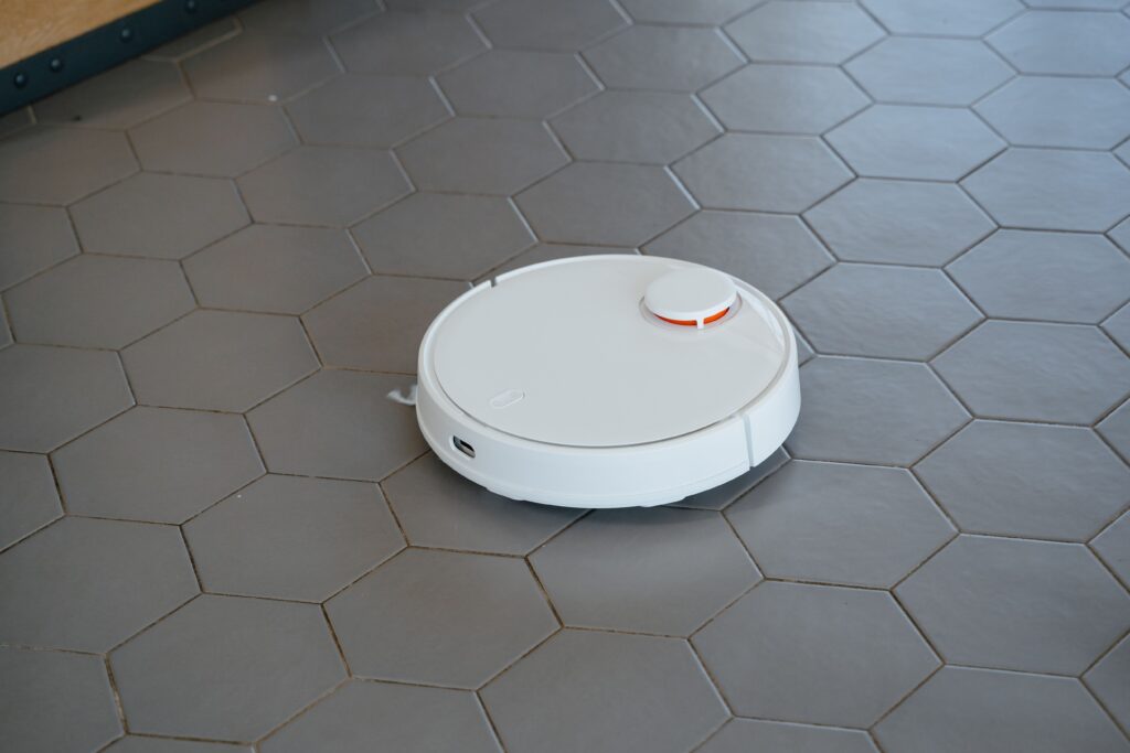 Shark PowerDetect UV Reveal : le robot aspirateur qui voit l’invisible A sleek, white robotic vacuum cleaner operating on a hexagonal tiled floor.